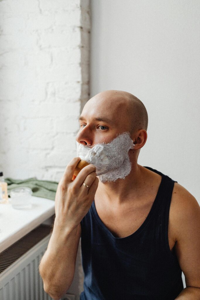Does Shaving Make Men's Acne Worse? Man shaving facial hair while checking skin for acne in bathroom mirror